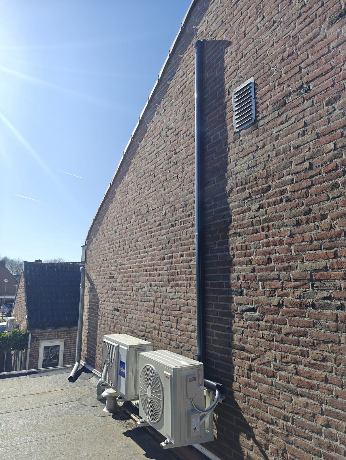 Twee buitenunits op beugels langs een lange bakstenen muur, de leidingen in een strakke goot omlaag